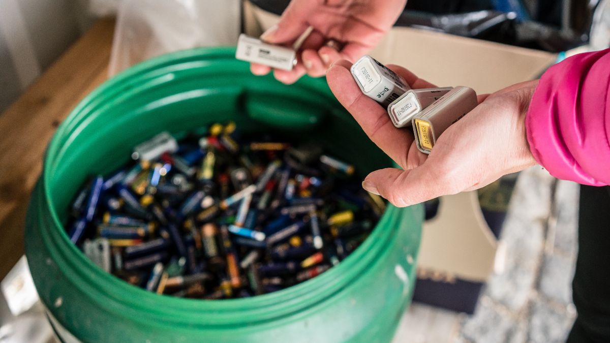 Eine Person gibt gebrauchte Batterien sachgerecht in einen großen grünen Sammelbehälter.